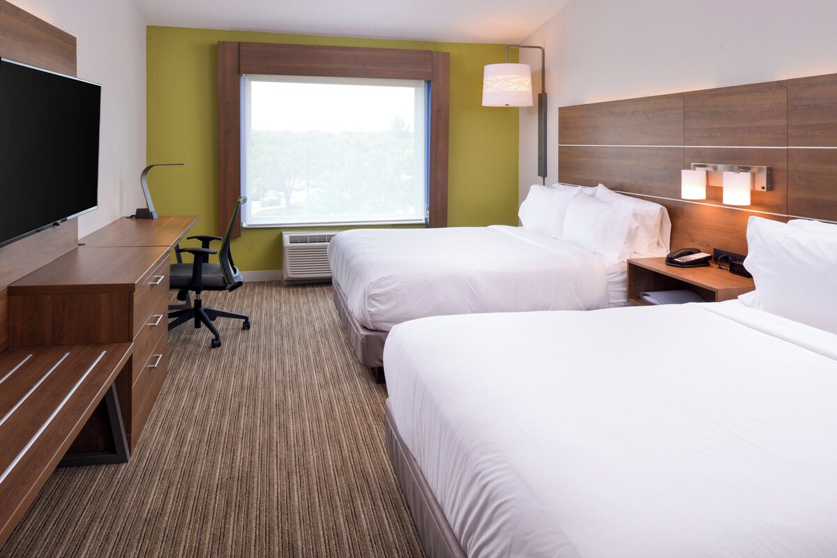 A hotel room with two beds, a desk, a chair, a TV, and a window with a view.