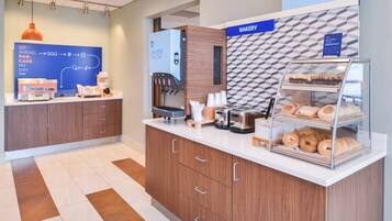 A modern breakfast area with a coffee machine, a pastry display, and a sign indicating a bakery.