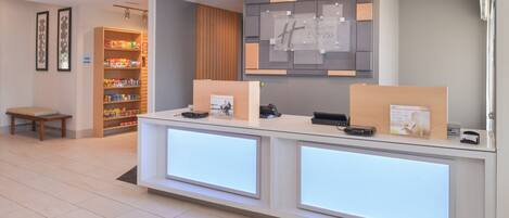 A hotel reception desk with a digital display, a seating area, and a snack bar.