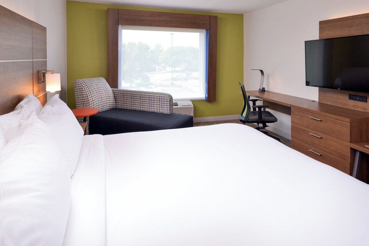 A hotel room with a bed, a desk, a chair, a television, and a window with a view of the outside.