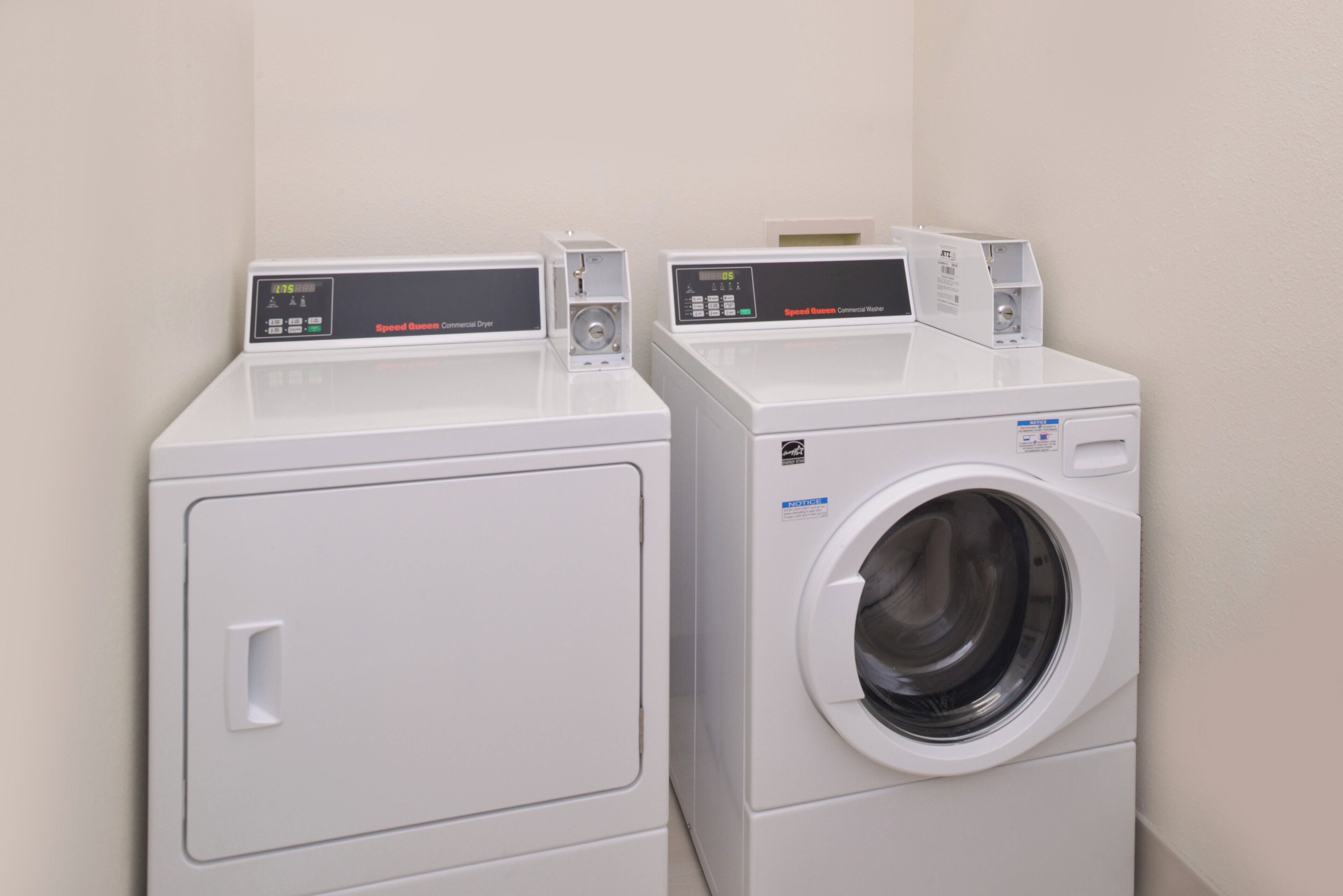 Two white commercial washers in a corner with a plain wall.