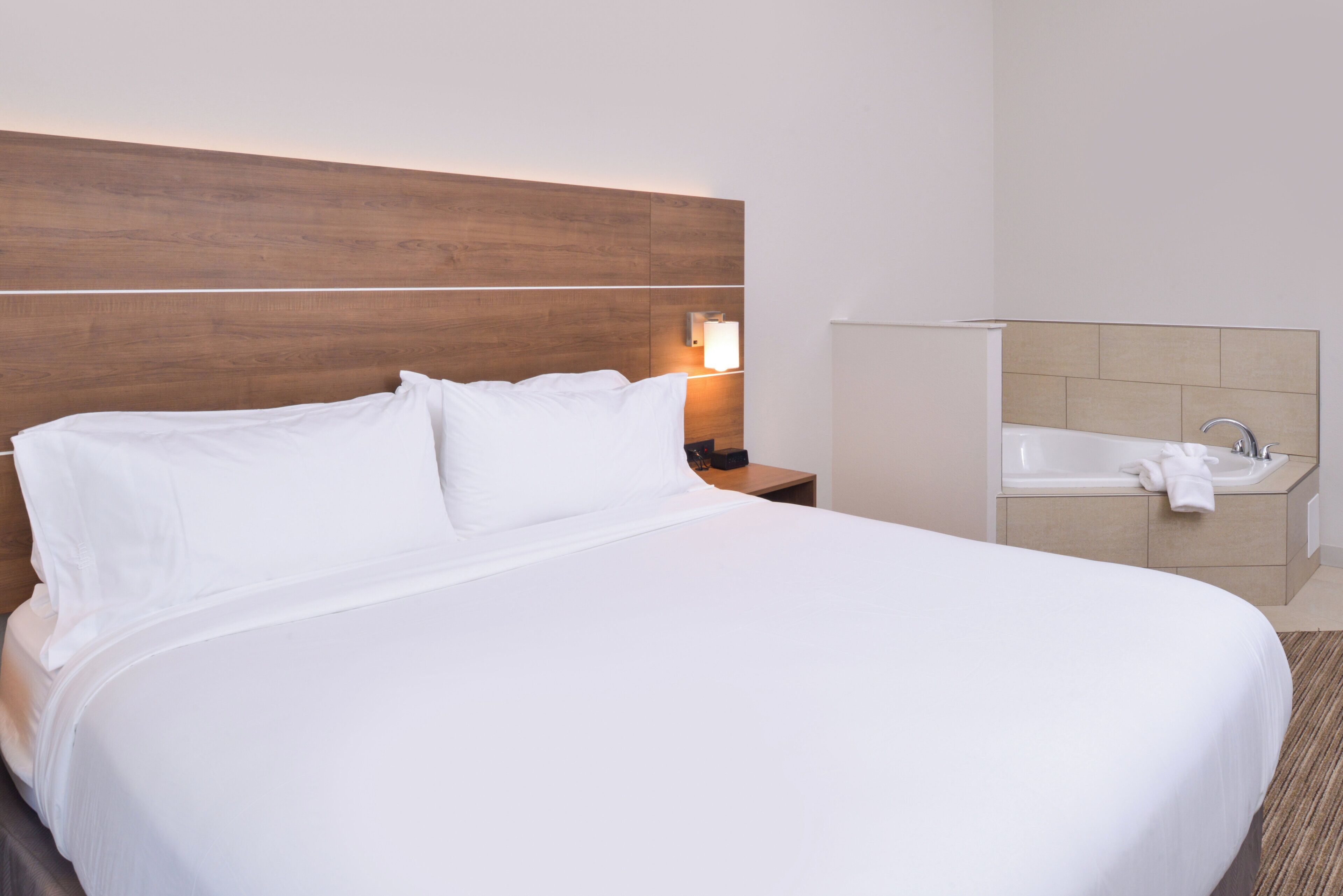 A hotel room with a large bed, a nightstand with a lamp, and a bathroom with a sink and mirror.