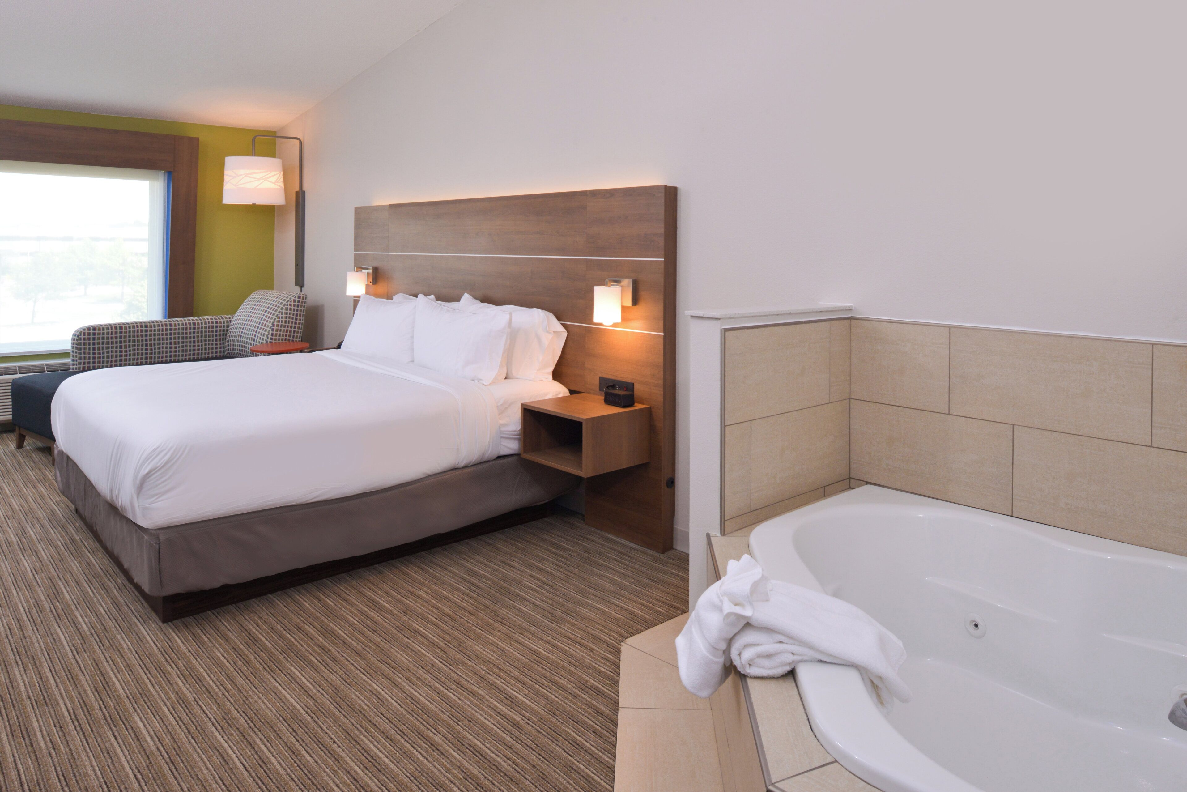A hotel room with a bed, bedside table, lamp, and a bathtub.