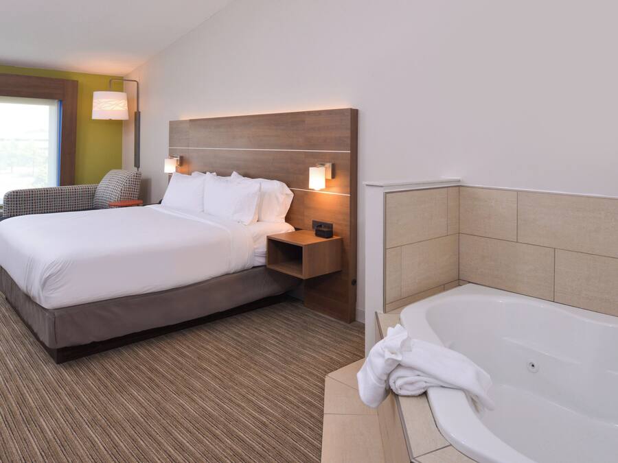 Une chambre d’hôtel avec un lit, une table de chevet, une lampe et une baignoire.