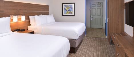 A hotel room with two beds, a wooden headboard, a framed artwork, a door, and a TV.