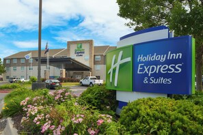 A Holiday Inn Express & Suites hotel with a prominent sign, a parking lot with cars, and a flagpole with the American flag. - Holiday Inn Express & Suites Omaha - 120th and Maple by IHG (Omaha)