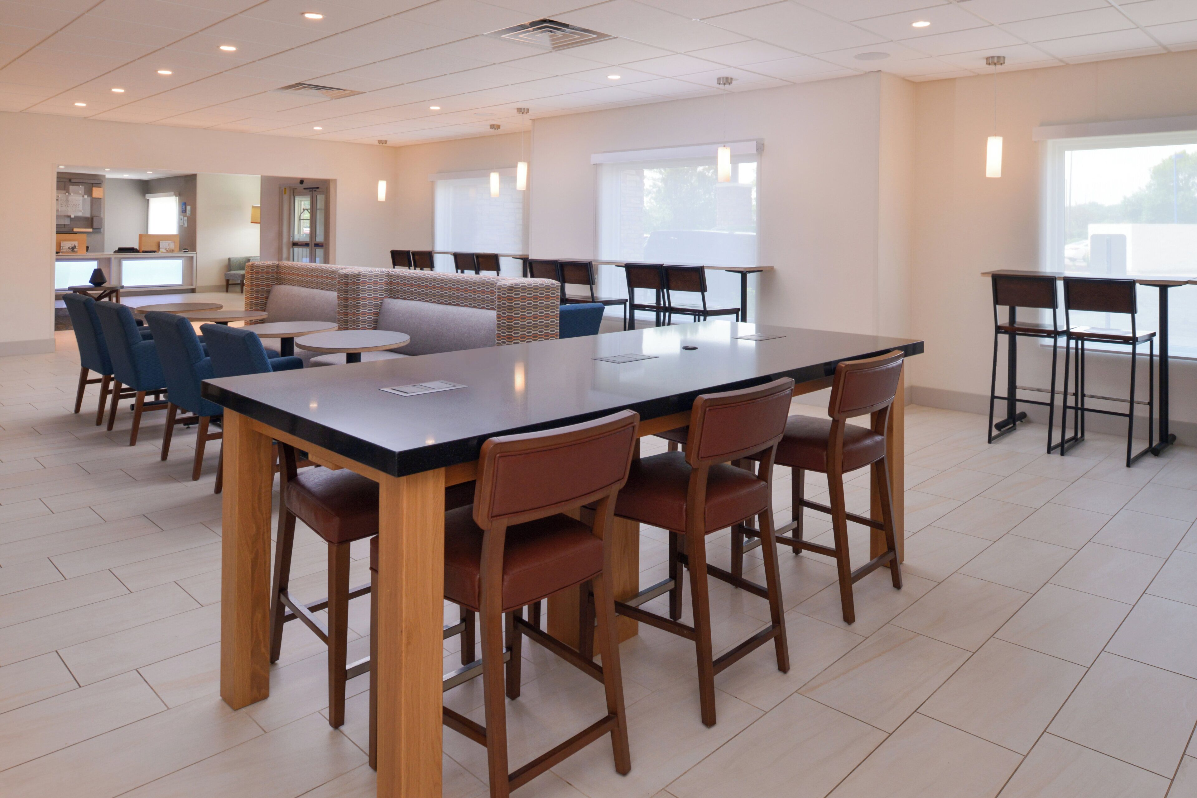A spacious indoor area with a large central table surrounded by chairs, a seating area with sofas, and a kitchen in the background.