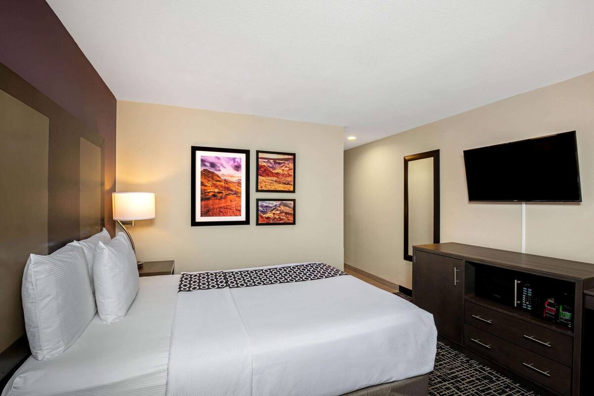 A hotel room with a large bed, a TV mounted on the wall, and a dresser.