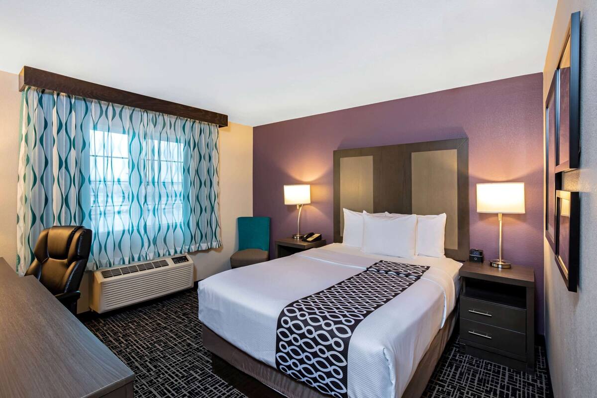 A hotel room with a large bed, two bedside lamps, a desk, and a chair.