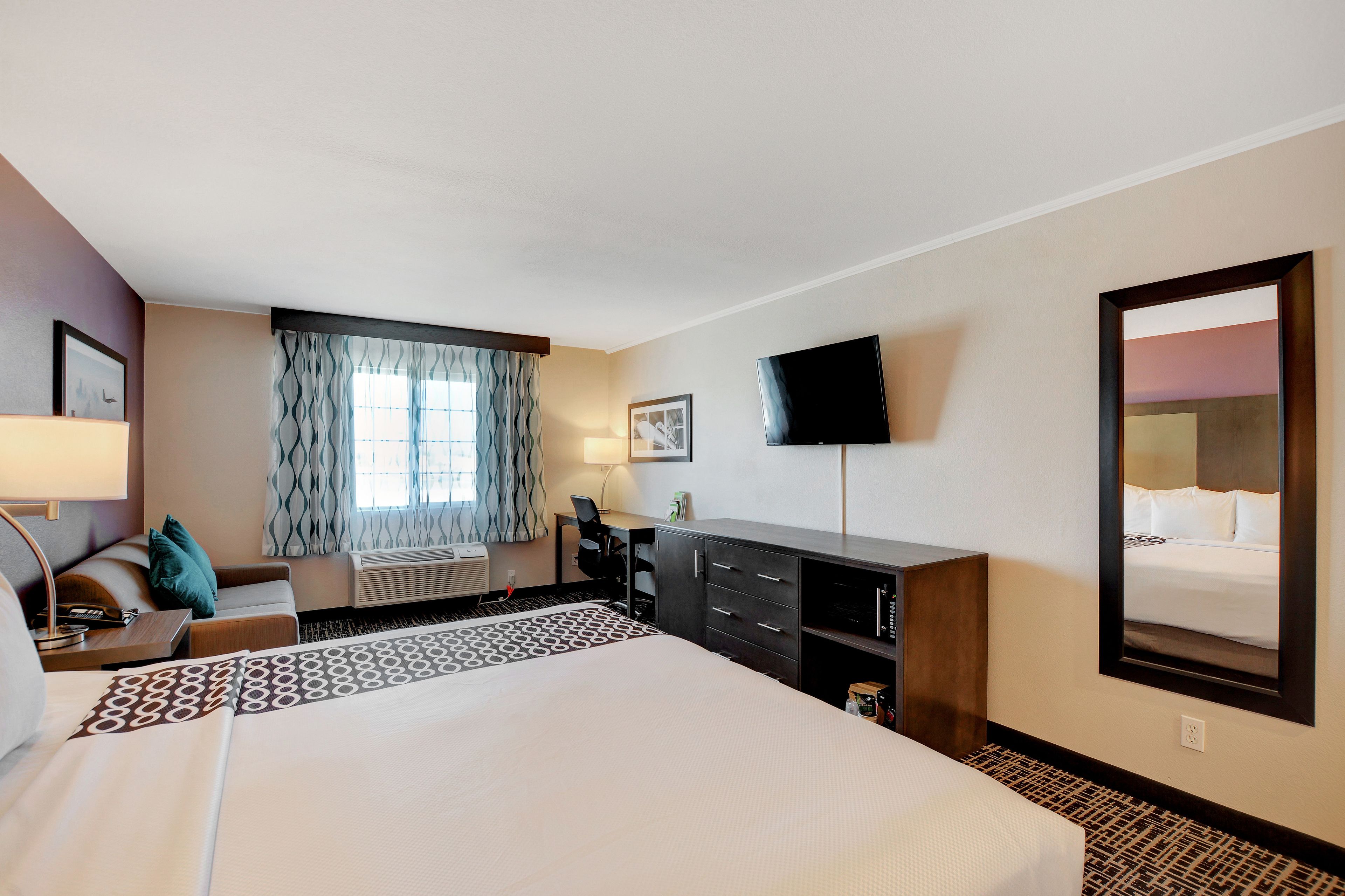 A hotel room with a large bed, a desk, a chair, a TV, and a window with curtains.