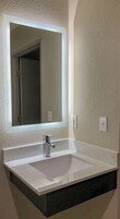 Un baño con lavamanos blanco, un espejo grande y una lámpara en la pared.