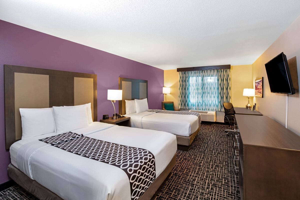 A hotel room with two beds, a desk, a TV, and a window with curtains.