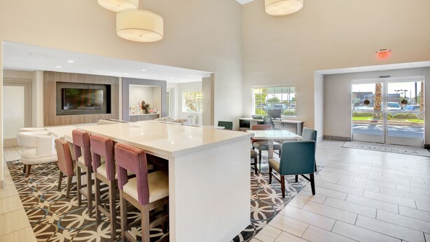 A modern hotel lobby with a central island bar, seating areas, and large windows offering views of the outside.