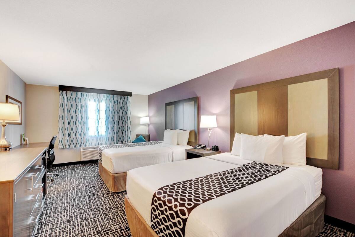 A hotel room with two beds, a desk, a chair, a mirror, and a patterned rug.