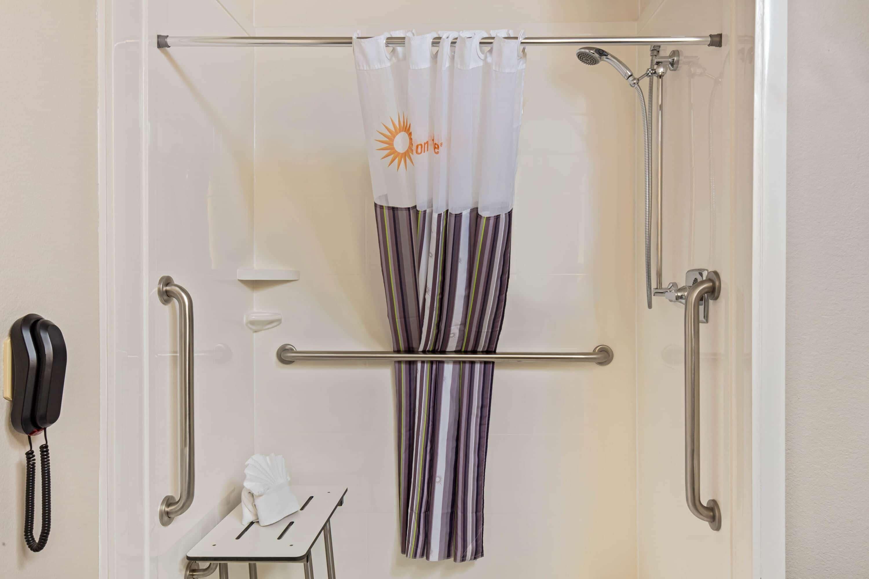 A shower area with a handrail, a towel rack, and a telephone.
