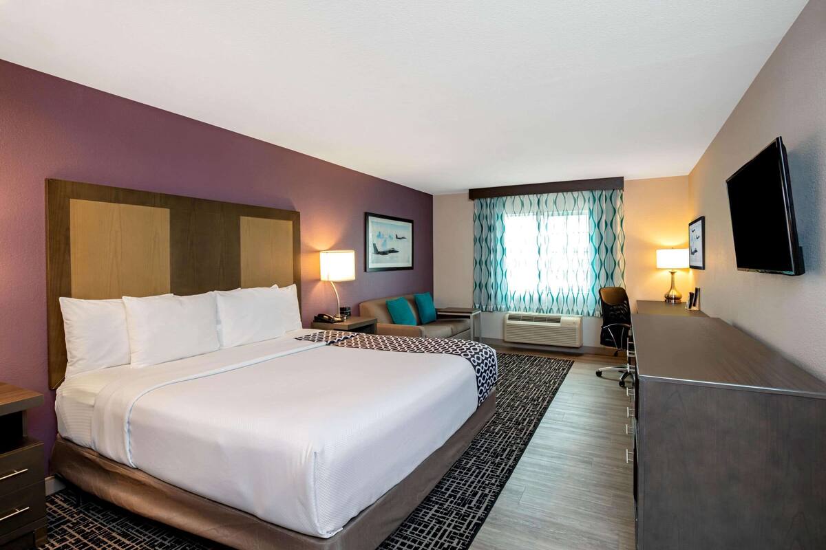 A hotel room with a large bed, a desk, a chair, a TV, and a window with curtains.