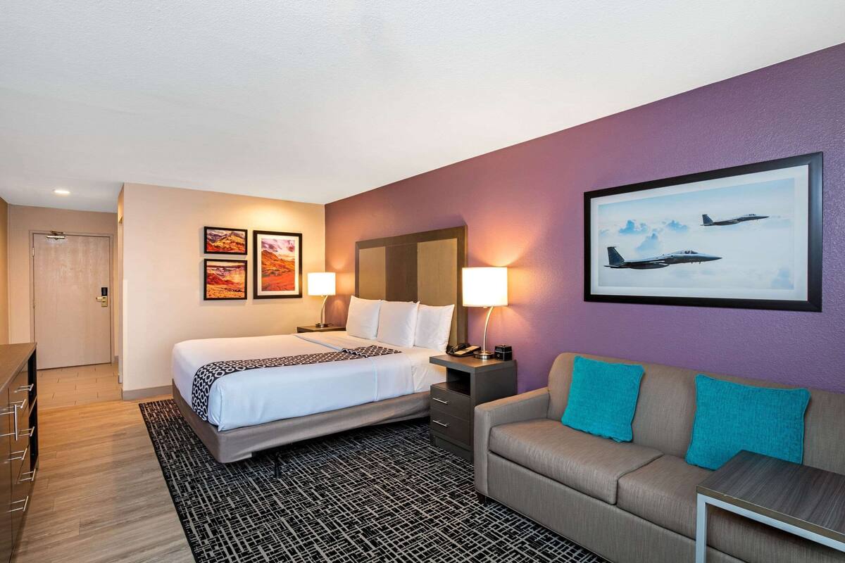 A hotel room with a bed, a sofa, a desk, and a wall-mounted TV.