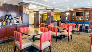 A hotel lobby with a bar area, seating with red and grey upholstered chairs, and a buffet counter with various food items. - Comfort Suites at Woodbridge (Avenel)