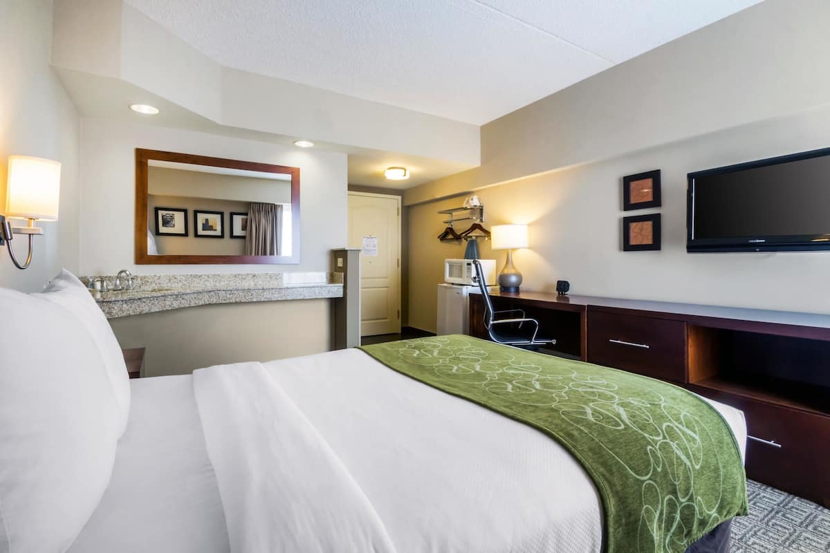 A hotel room with a bed, a desk, a television, a mirror, and a bathroom.