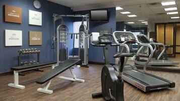 A gym with exercise equipment, a bench, dumbbells, and motivational posters on the wall.
