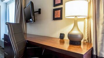 Une chambre d’hôtel avec un bureau en bois, une chaise, un téléviseur fixé au mur, une lampe et deux tableaux encadrés.