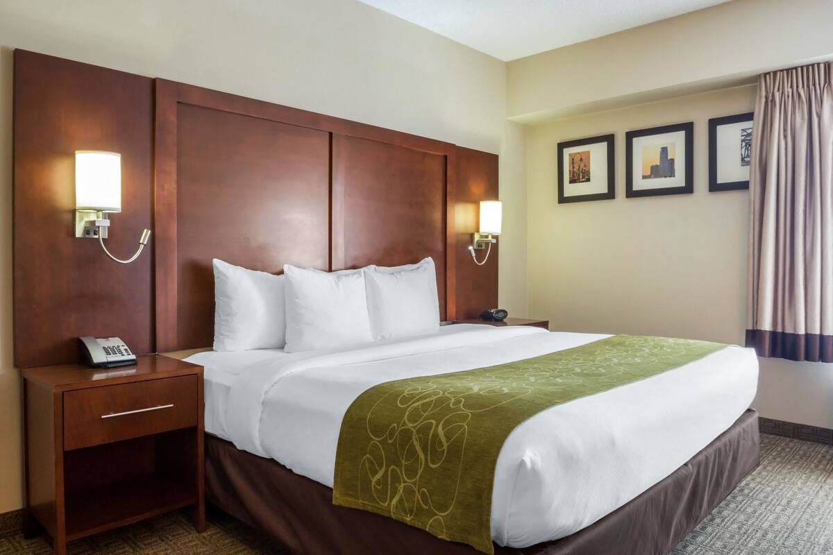 A hotel room with a large bed, two bedside tables, a telephone, wall-mounted lights, and framed pictures on the wall.