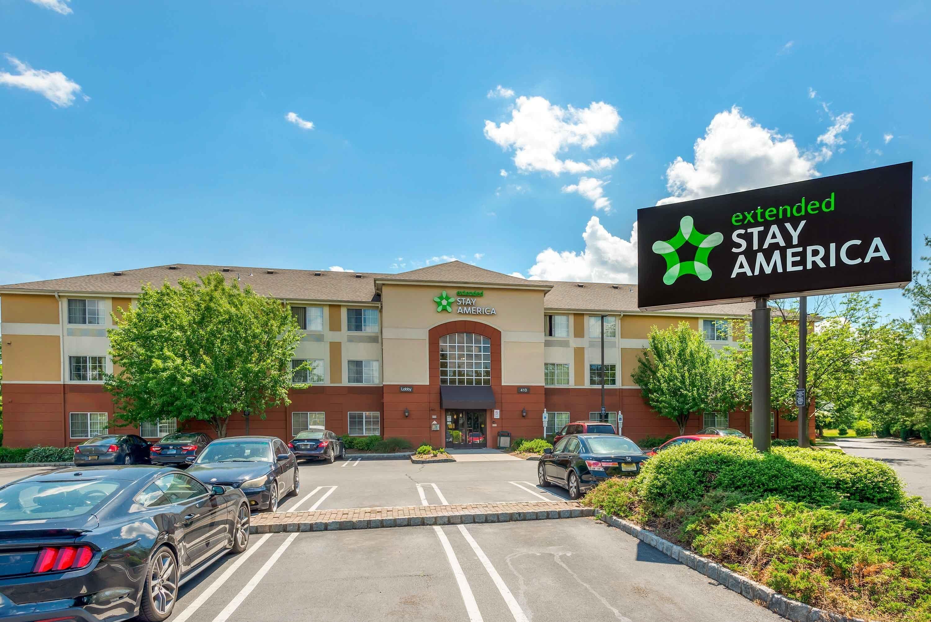 Een Stay America hotel met een parkeerplaats, een heldere lucht en een bord.