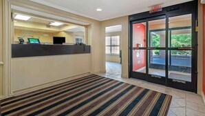 Un'area della reception di un hotel, con una scrivania, uno schermo digitale e un tappeto a righe che conduce a una porta d'uscita.
