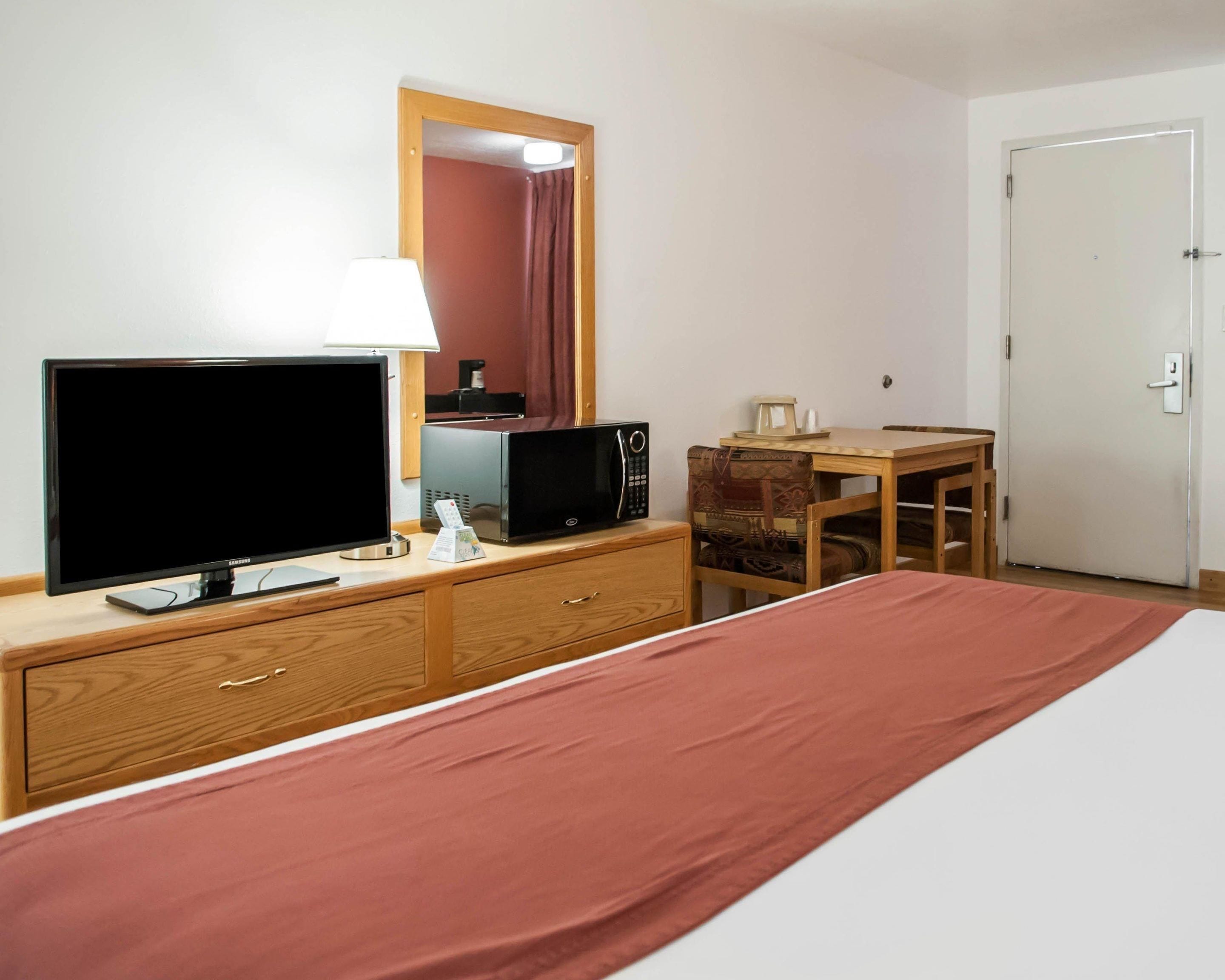 Habitación de hotel con cama, televisión, microondas, cafetera, escritorio de madera y puerta.