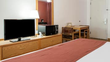 Habitación de hotel con cama, televisión, microondas, cafetera, escritorio de madera y puerta.