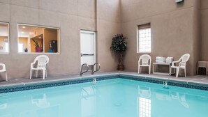 Una piscina interior con agua azul cristalina, rodeada de paredes color beige y sillas de plástico blanco.