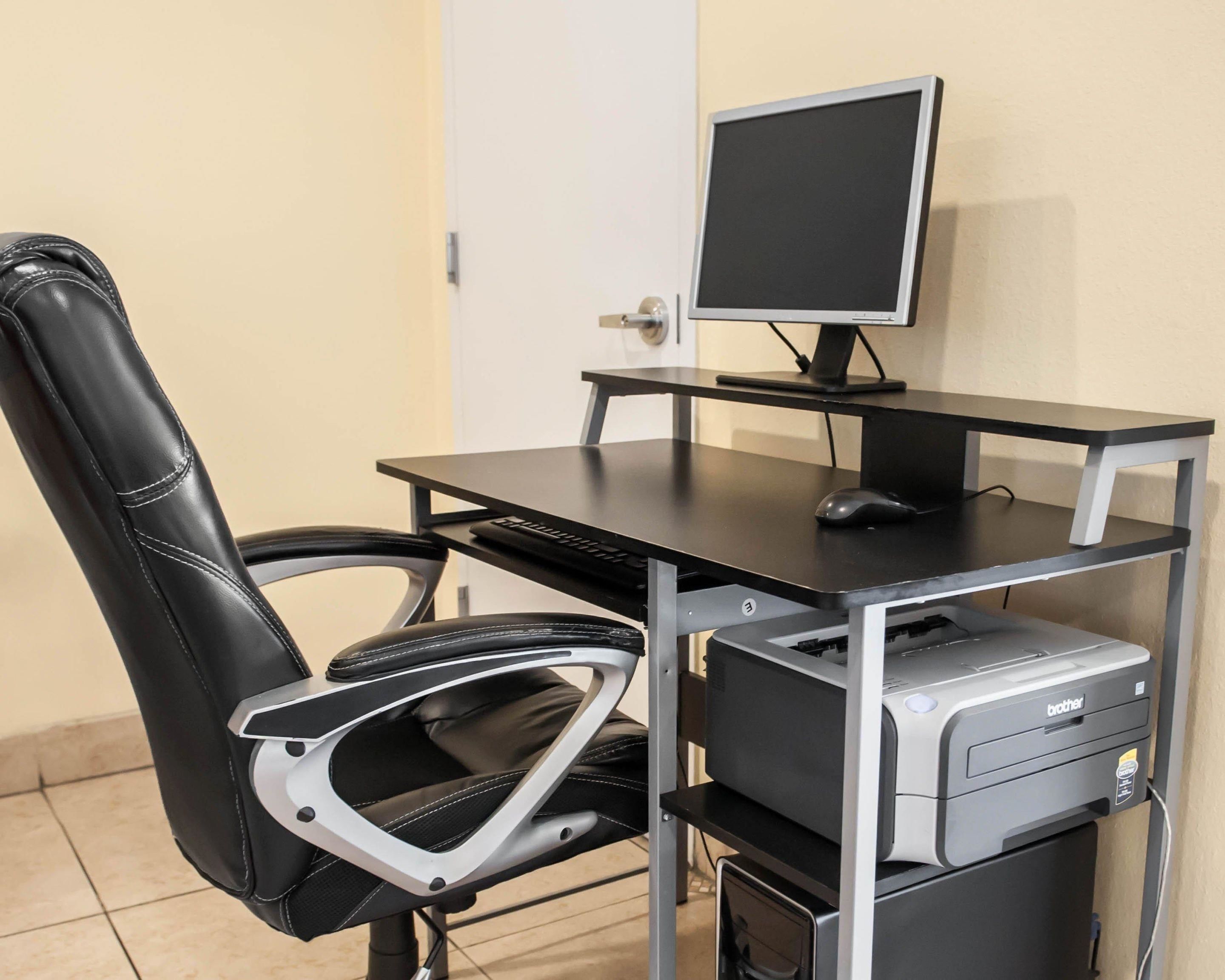 Ein schwarzer Bürostuhl mit hoher Rückenlehne, ein schwarzer Schreibtisch mit Monitor, Tastatur und Maus, sowie ein Brother-Drucker auf einem Metallständer.