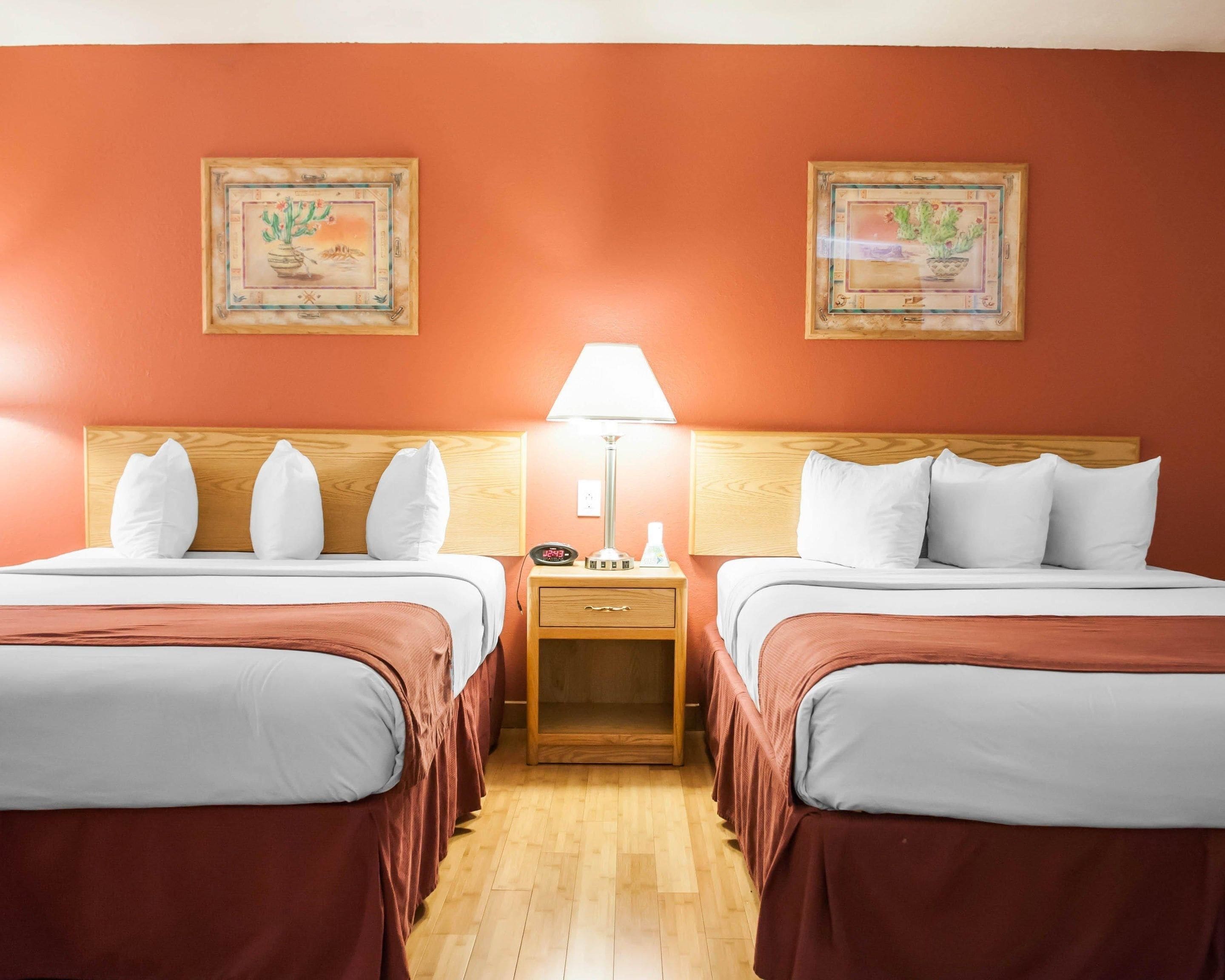 A hotel room with two beds, a nightstand with a lamp, and two framed pictures on the wall.