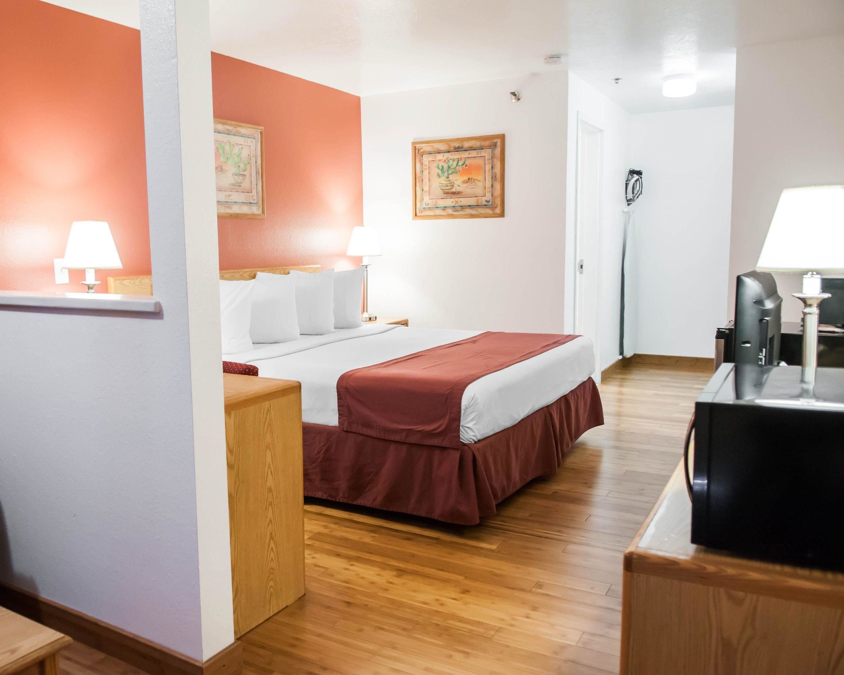 Quarto de hotel com cama, escrivaninha, cadeira, abajur e um quadro na parede.