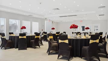 A conference room with round tables, black chairs with gold sashes, and red flowers on each table.