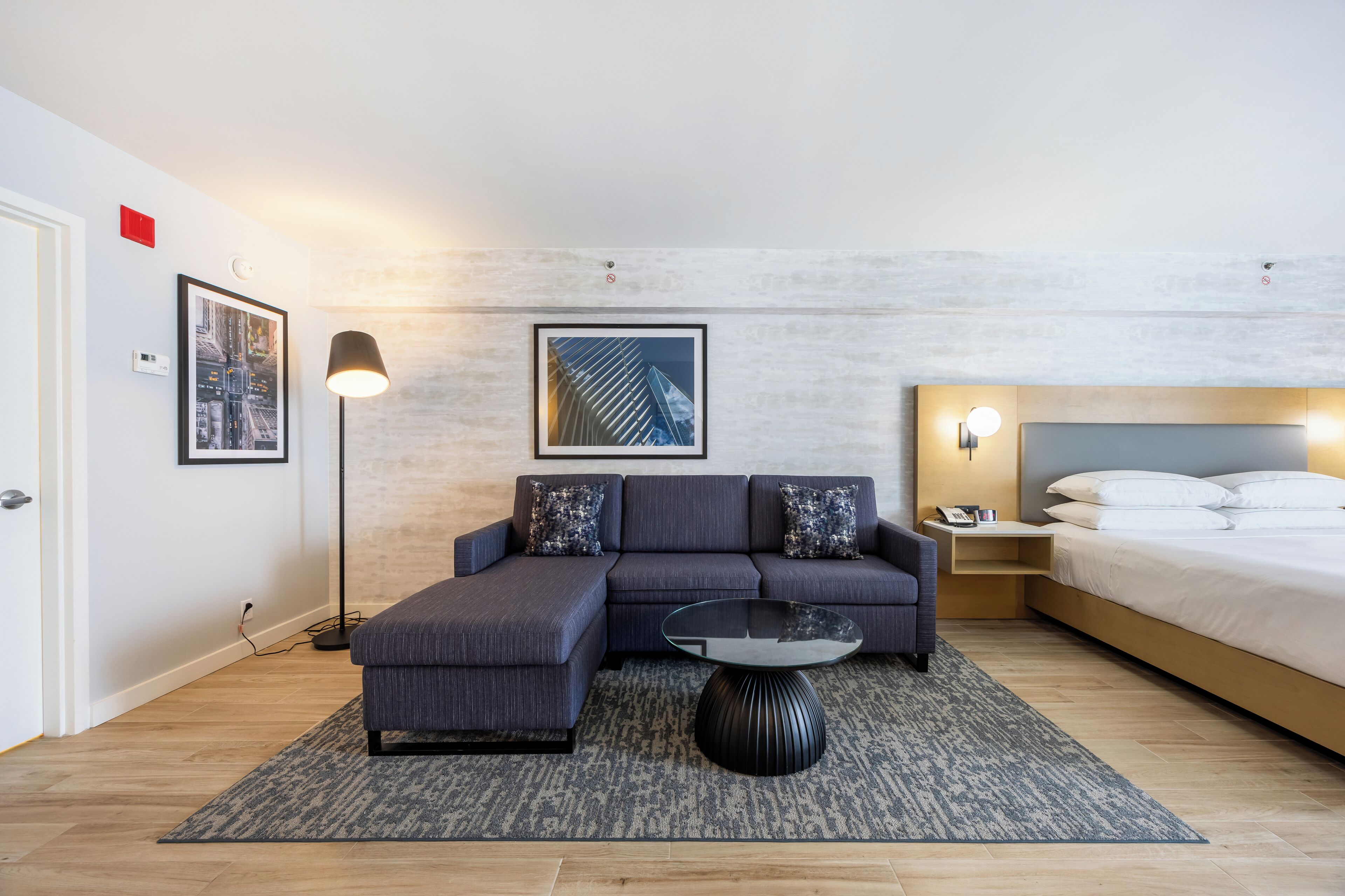 Una habitación de hotel moderna con sofá modular, una mesa de centro redonda, cama y obras de arte en las paredes.