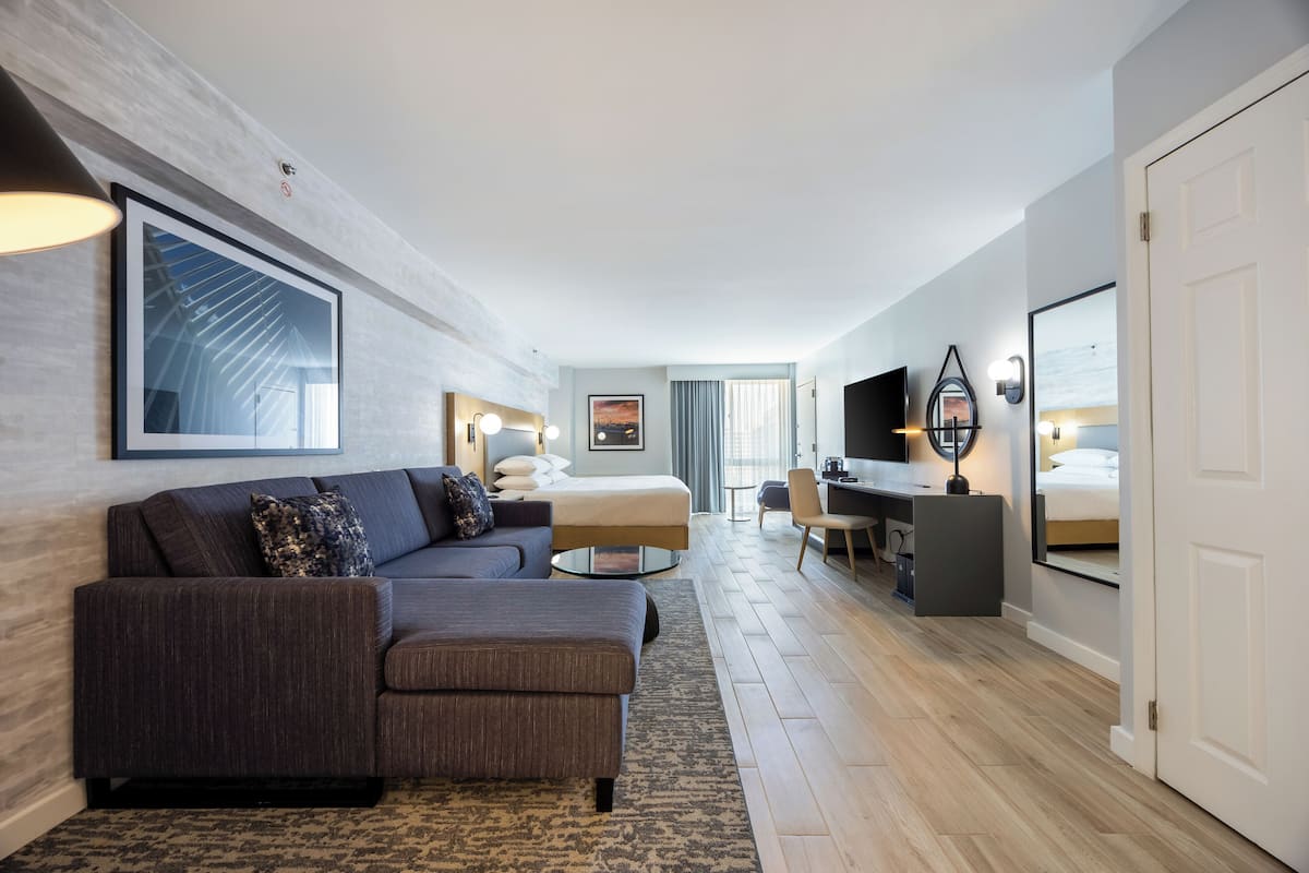 Una habitación de hotel moderna con un sofá modular, una cama, un escritorio y un televisor.
