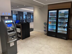 An ATM machine, a reception desk, and a beverage refrigerator in a hotel lobby.