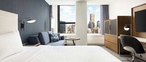 Habitación de hotel con una cama grande, un sofá, un escritorio, una silla, un televisor y vistas a la ciudad.