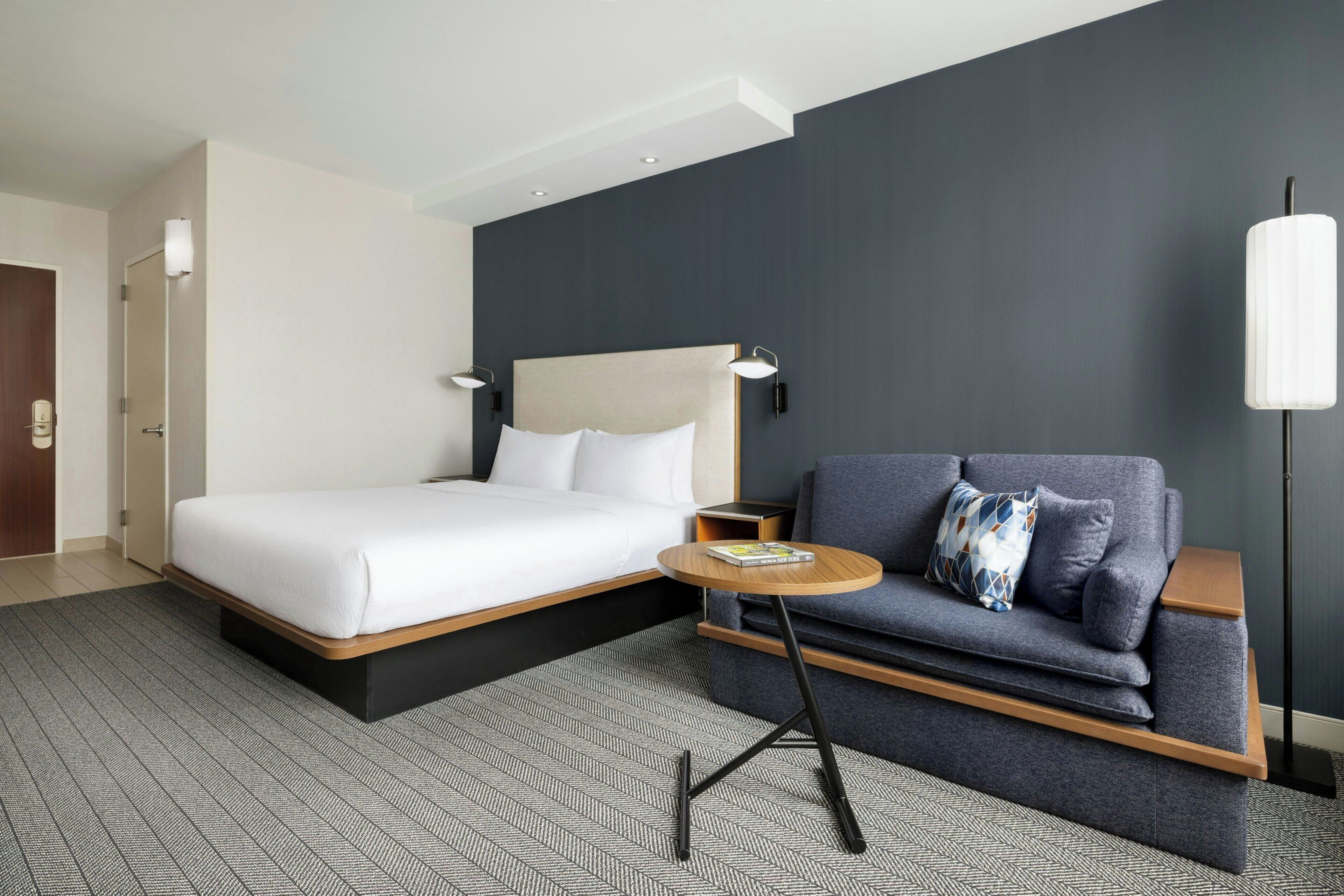Une chambre d’hôtel moderne équipée d’un lit, d’un canapé, d’une petite table et d’un lampadaire.