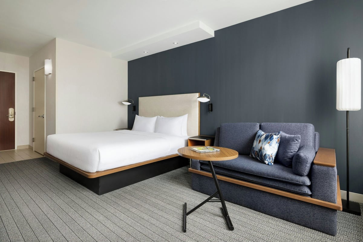 A modern hotel room with a bed, a sofa, a small table, and a floor lamp.