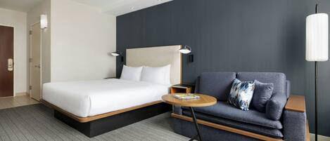 A modern hotel room with a bed, a sofa, a small table, and a floor lamp.