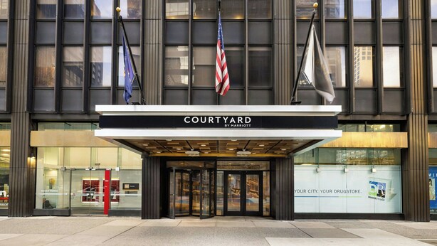 L’entrée d’un hôtel avec une façade en verre, une enseigne indiquant « COURTYARD BY MARRIOTT » et des drapeaux.