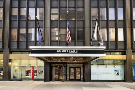 A hotel entrance with a glass facade, a sign reading 'COURTYARD BY MARRIOTT,' and flags.. Courtyard New York Manhattan/ Midtown East