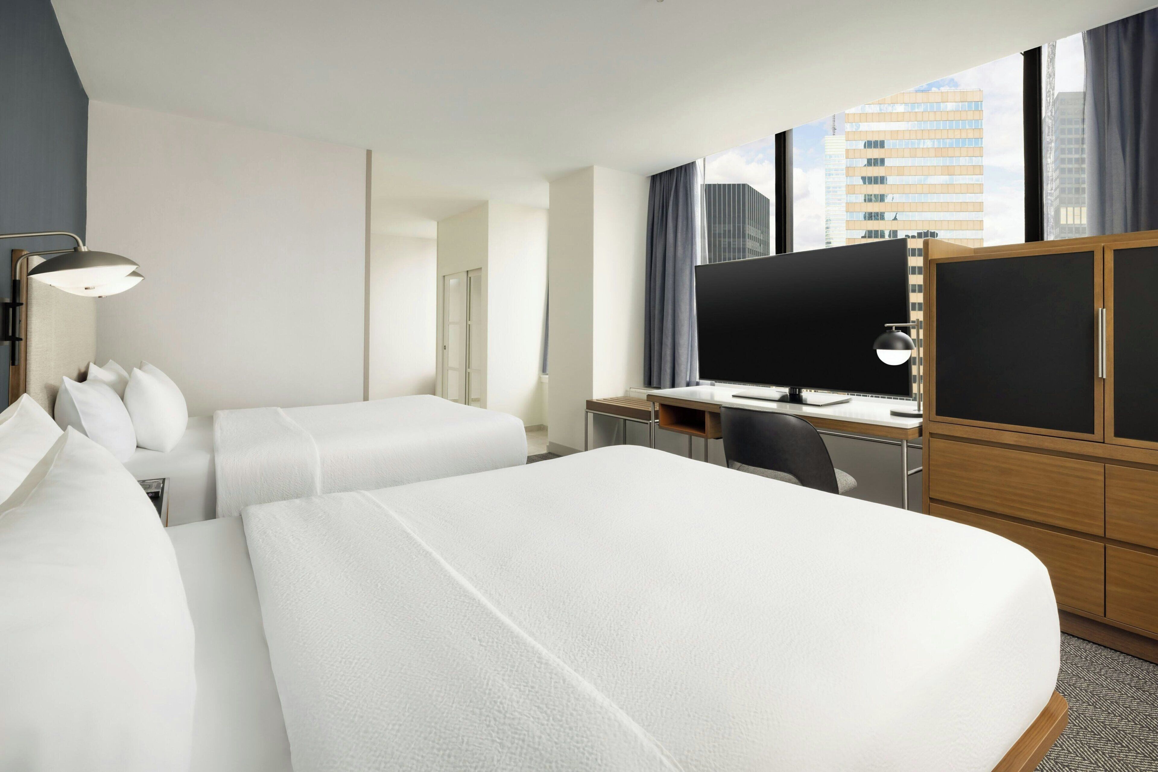 Habitación de hotel con dos camas, un escritorio con computadora, un televisor y un armario.