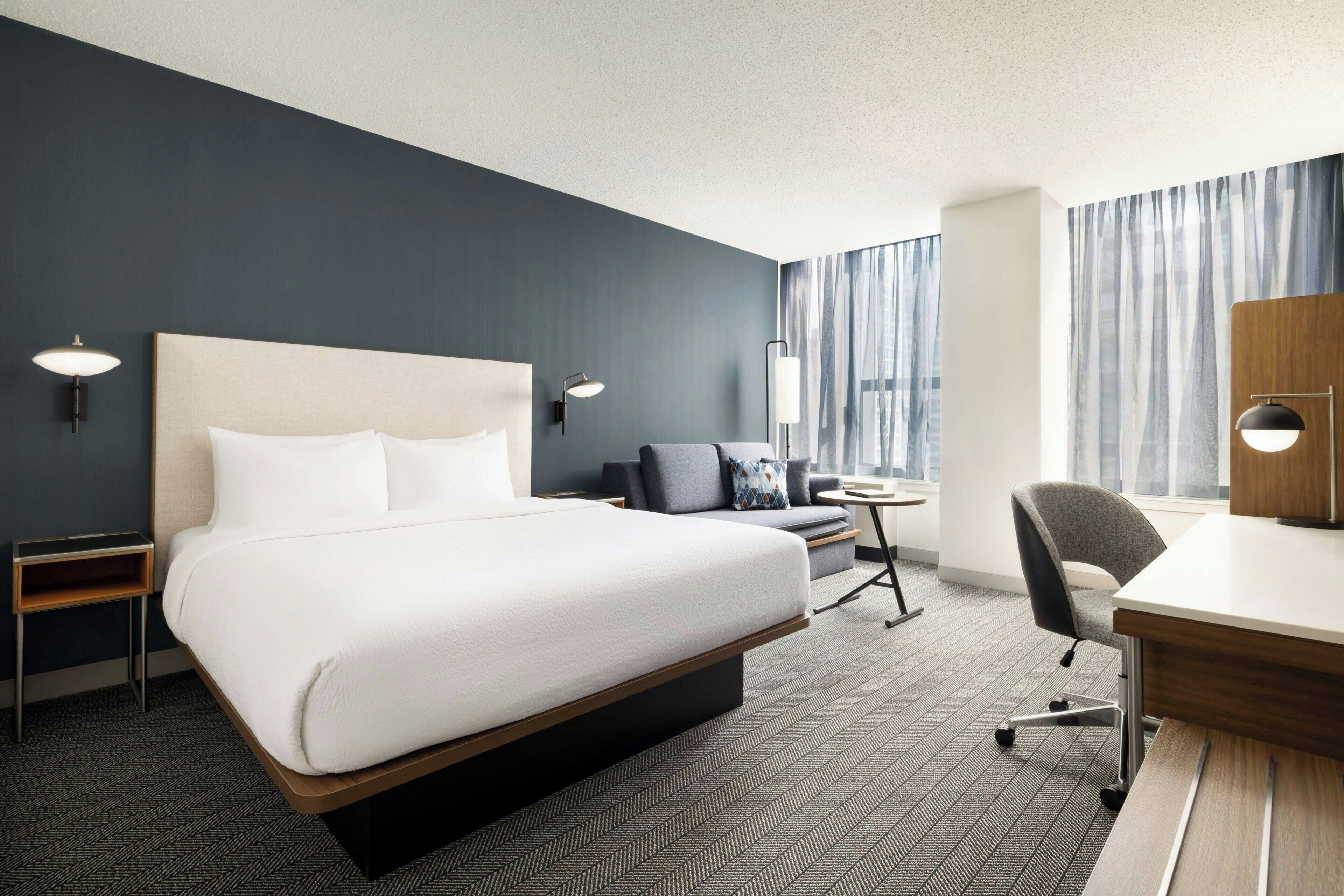 Een moderne hotelkamer met een groot bed, een bureau, een stoel en een klein tafeltje.