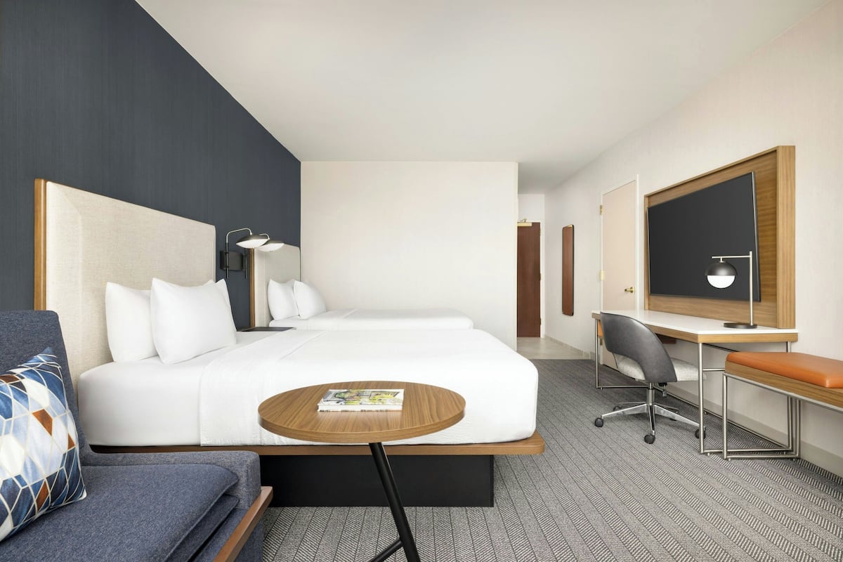 A hotel room with a bed, a desk, a chair, a small table, and a television.