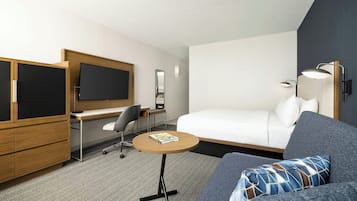 Quarto de hotel moderno com cama, escrivaninha, cadeira, mesa redonda, televisão e abajur.