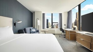 Une chambre d’hôtel avec un grand lit, un bureau, une chaise, une petite table et une vue sur le paysage urbain.