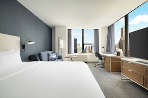 Habitación de hotel con una cama grande, un escritorio, una silla, una mesita y vistas a la ciudad.